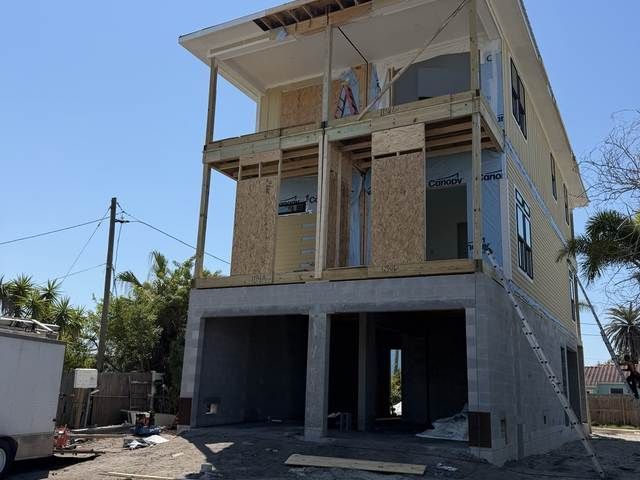 Two-story unfinished house under construction with exposed concrete, brick walls, and open garage space.
