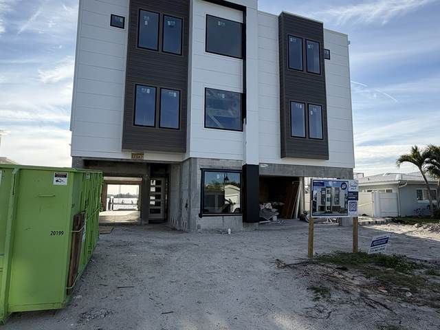 Three-story modern apartment building under construction with a gravel driveway and green dumpster in front