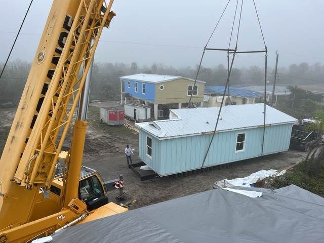 Crane lifting a light blue mobile home at a foggy construction site.