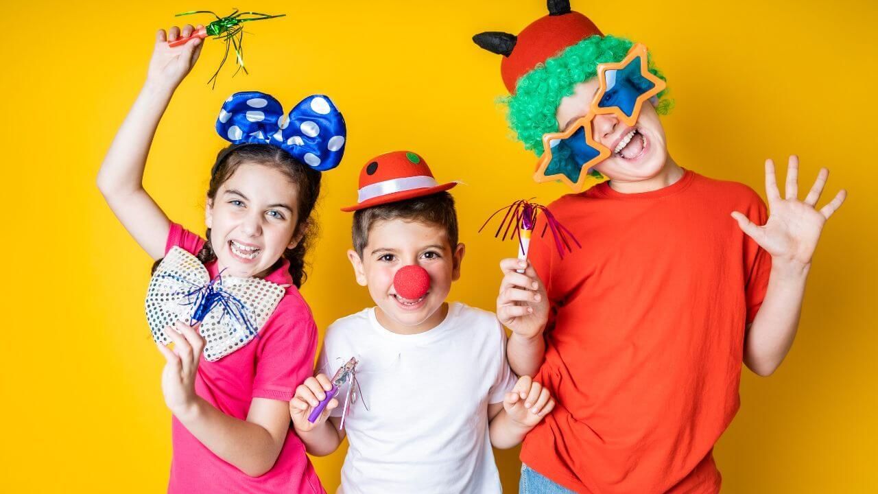 Three children are dressed up as clowns and holding balloons.