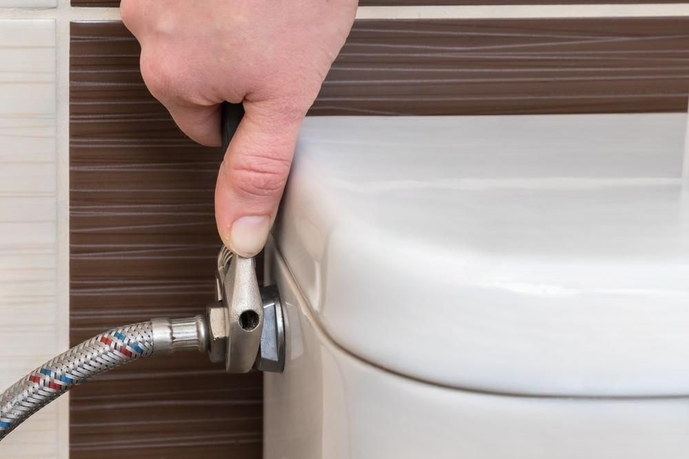 A person is fixing a toilet with a wrench.