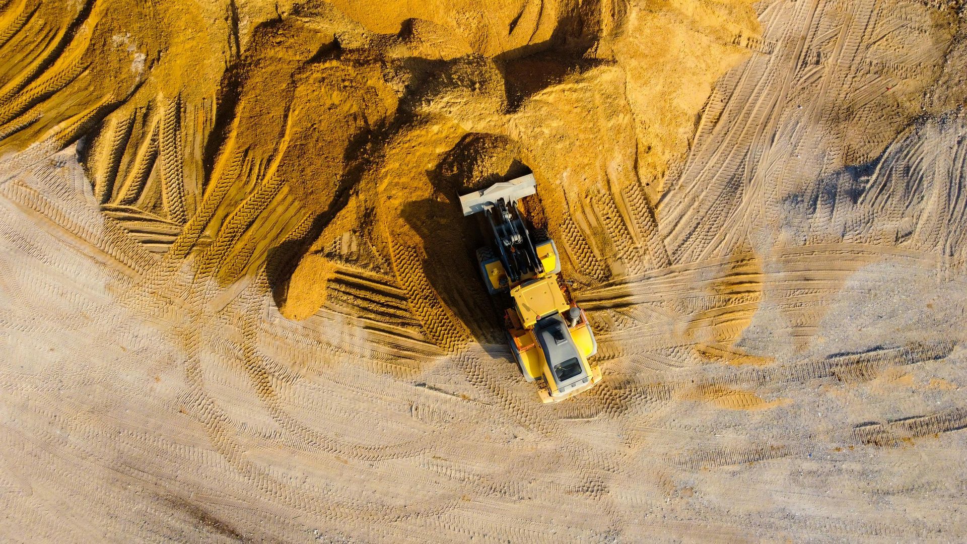 Yellow bulldozer working on a pile of yellow sand, viewed from above at a construction site.
