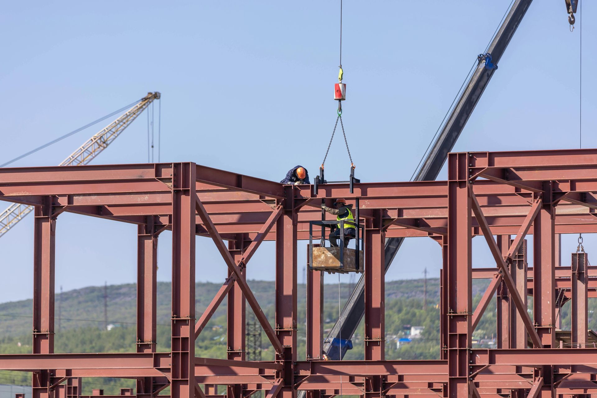 Construction workers assembling steel beams on a sunny day. Crane lifting a beam.