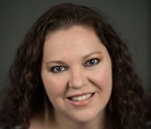 Woman with brown curly hair smiles, looking directly at the camera.