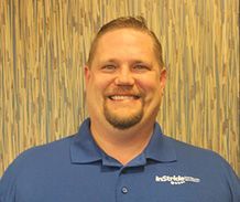 Smiling man with a goatee, wearing a blue polo shirt, in front of a patterned background.