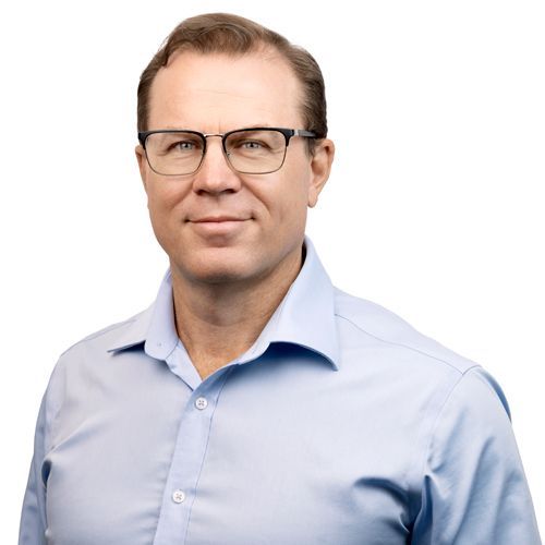 A man wearing glasses and a light blue shirt is smiling for the camera.