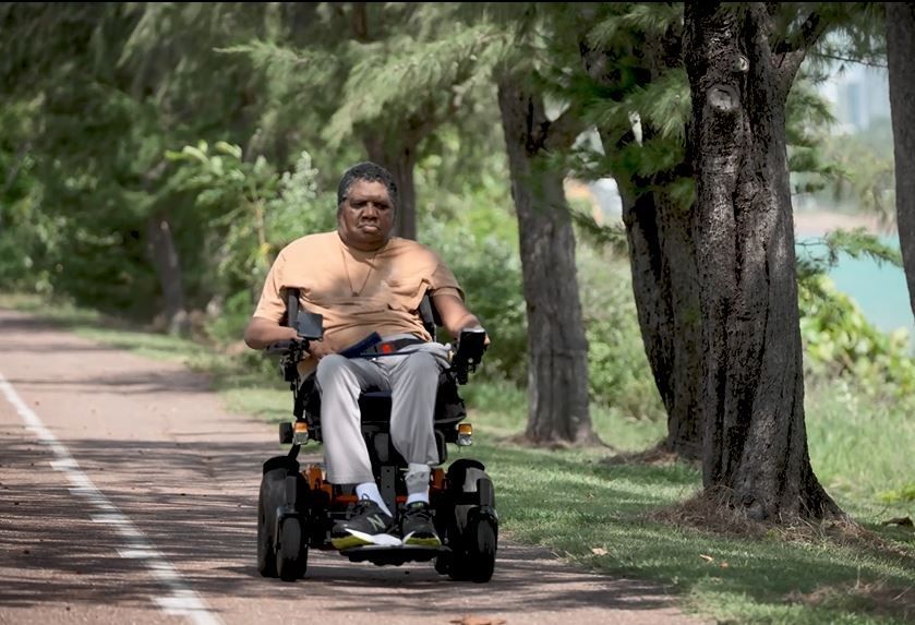 A man in a wheelchair is riding down a path.