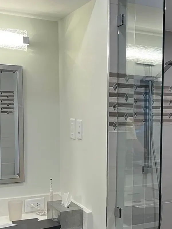 Bathroom with glass shower door, light fixtures, and neutral-colored walls.