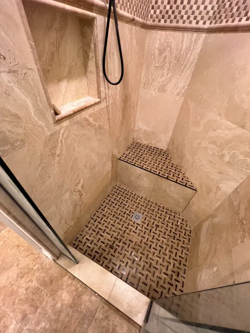 Shower stall with beige tile, corner bench, and small stone floor tiles.