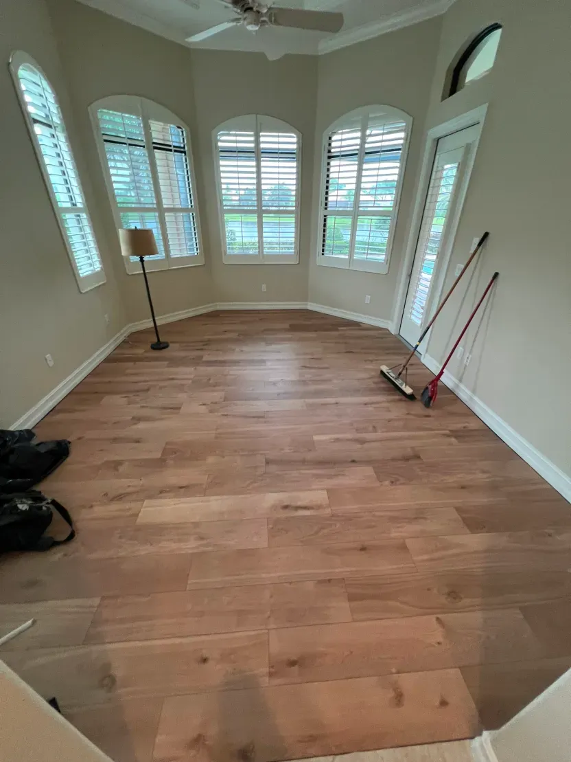 A room with new wood flooring, three arched windows, and cleaning supplies. Beige walls.