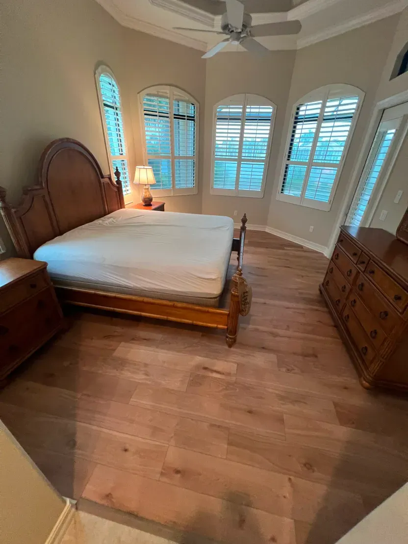 Bedroom with hardwood floors, bed, dresser, nightstand, and shuttered windows.