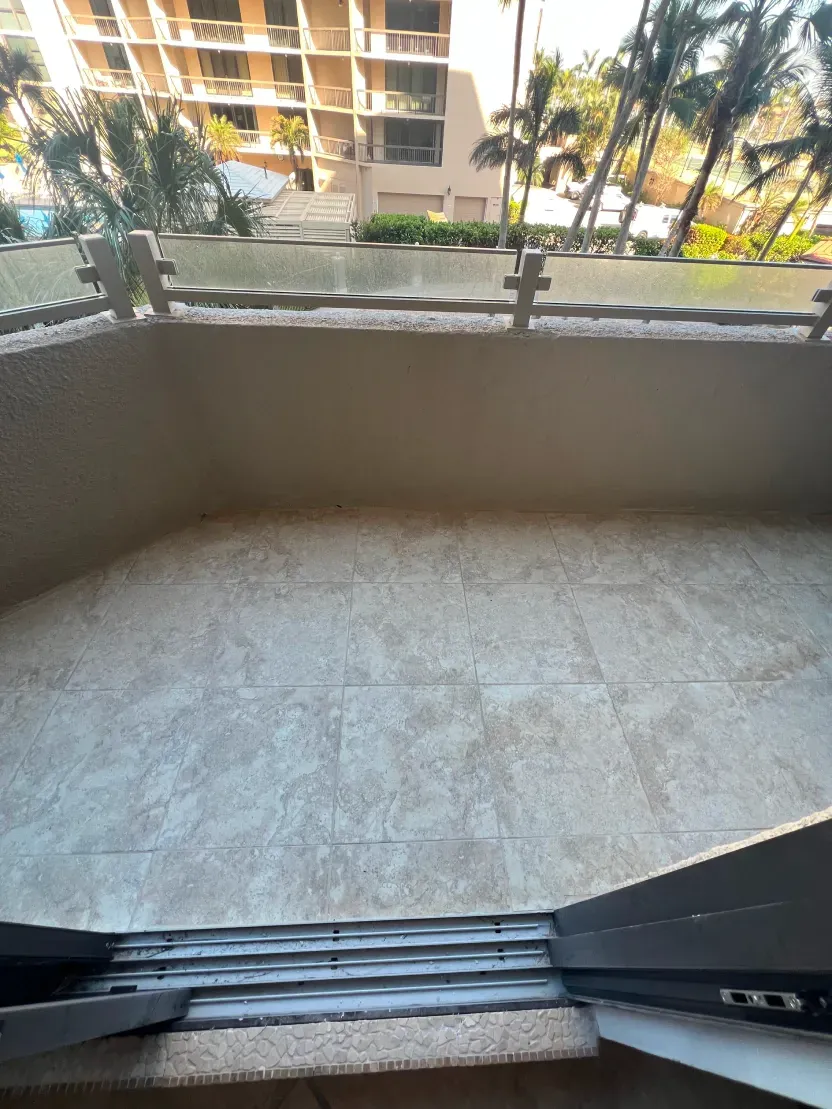 Balcony with beige tiled floor, tan wall, and a view of buildings and palm trees.