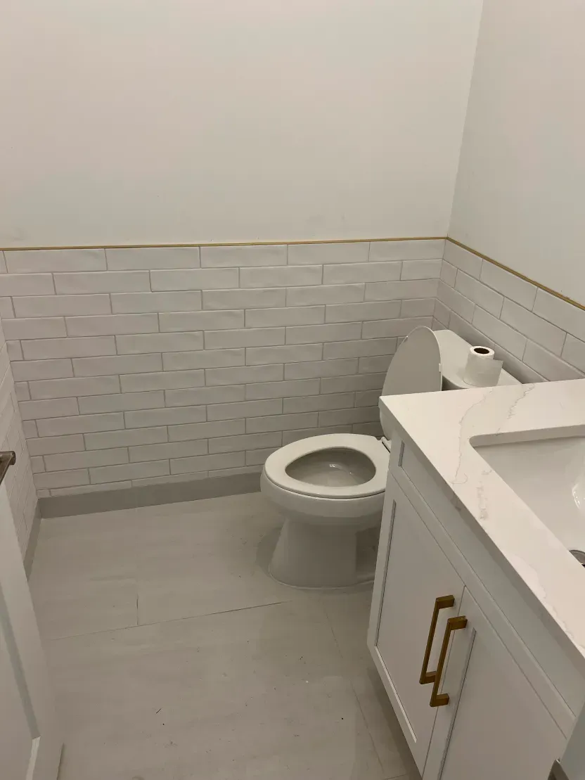 White bathroom with toilet, vanity, and textured tile wall.