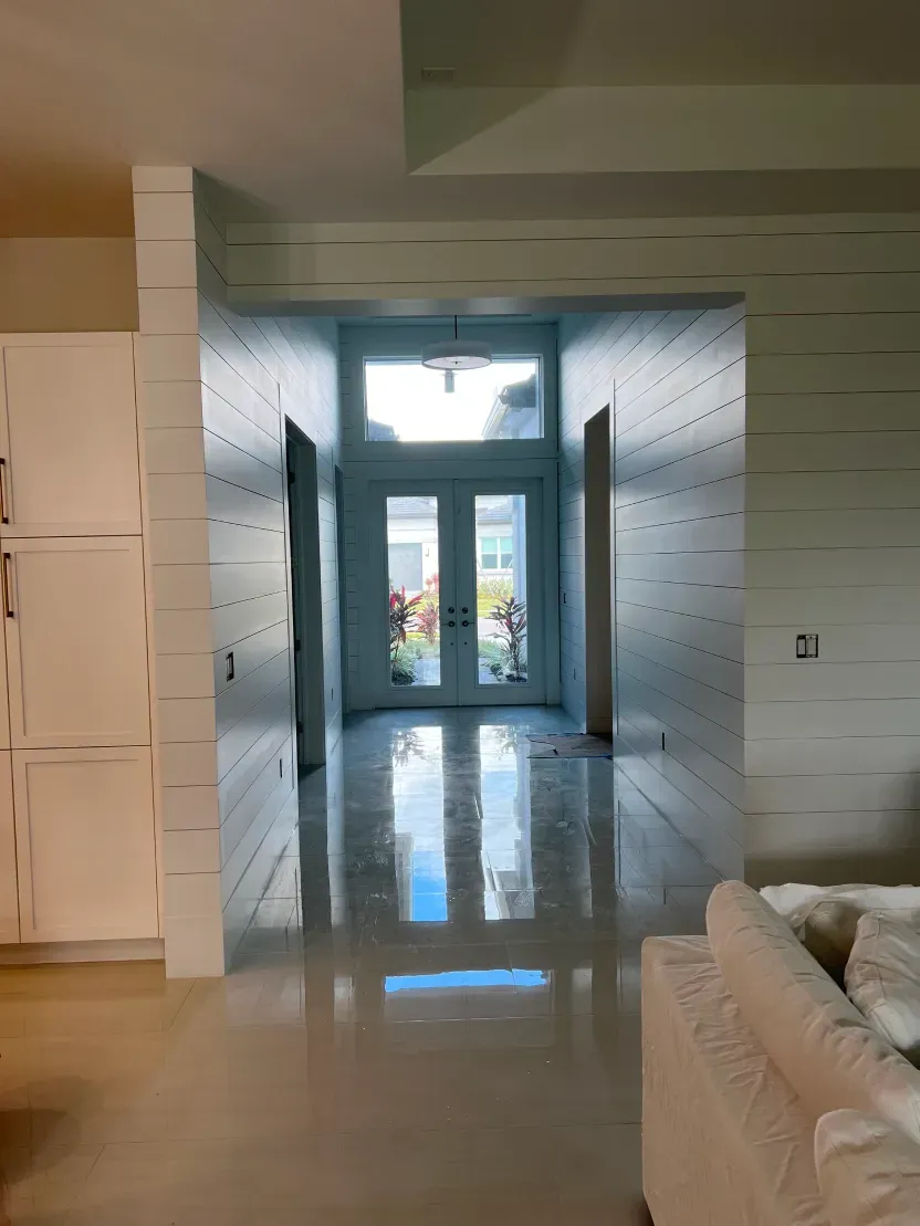 Bright hallway with white walls and flooring leading to glass double doors.