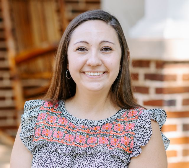 A woman is smiling for the camera in front of a brick building.