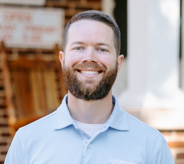 A man with a beard is smiling for the camera while wearing a blue shirt.