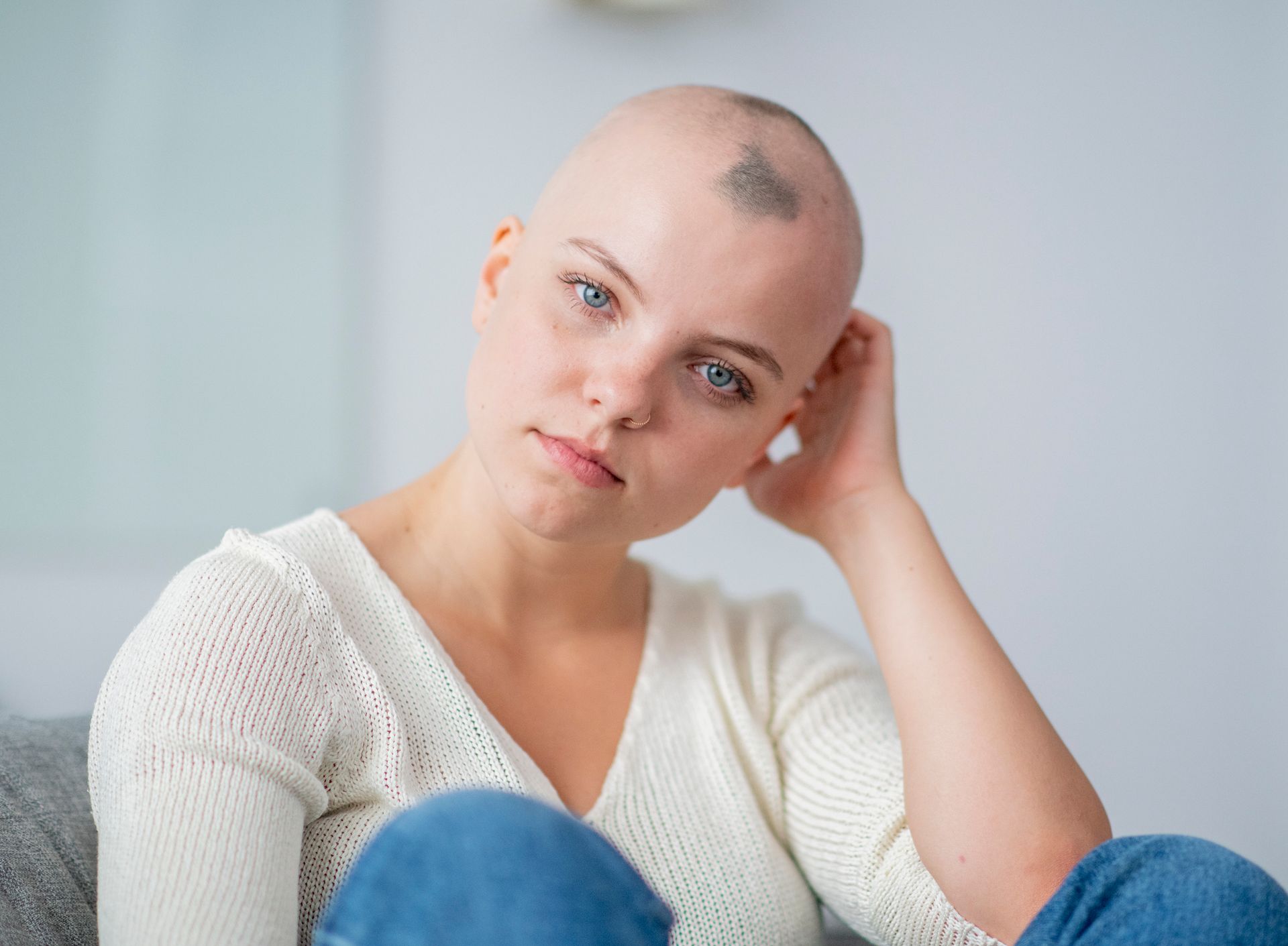 Una donna calva con un tatuaggio sulla testa è seduta su un divano.