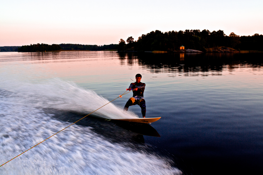 A man is wakeboarding on a lake at sunset.