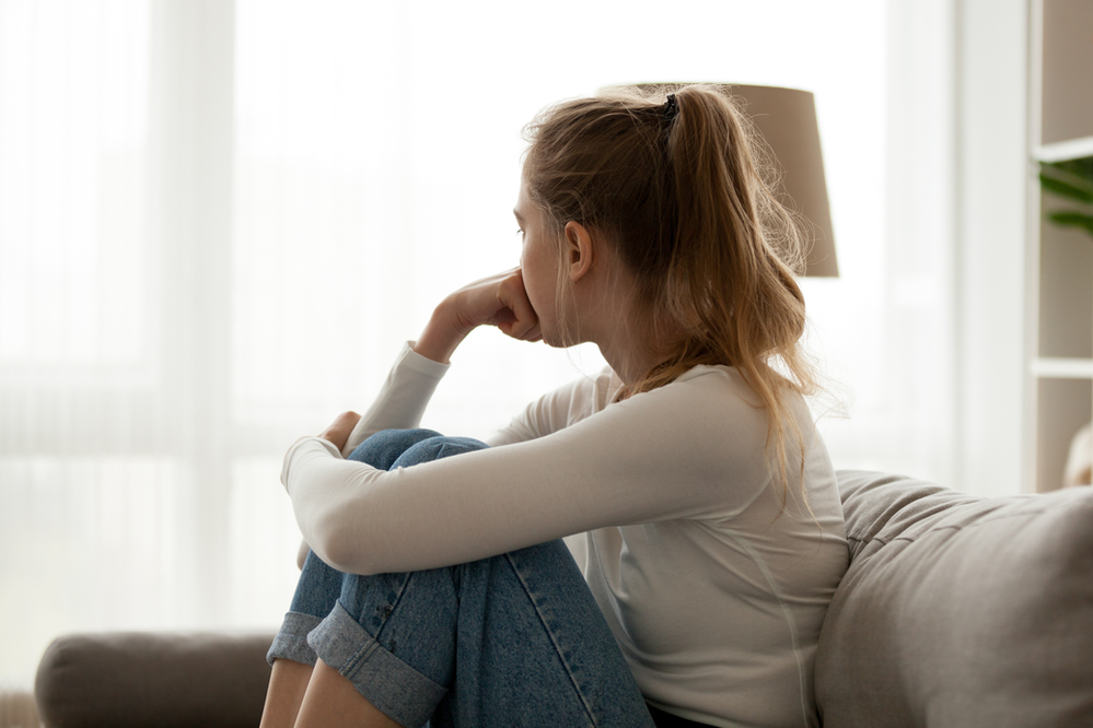 A woman is sitting on a couch with her legs crossed and looking out the window.