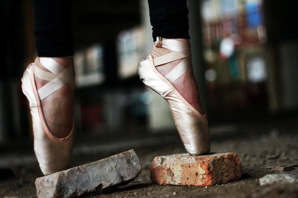 A close up of a person wearing pointe shoes standing on a brick.