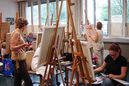 Des gens peignent sur des chevalets dans un atelier d'art lumineux avec des fenêtres.