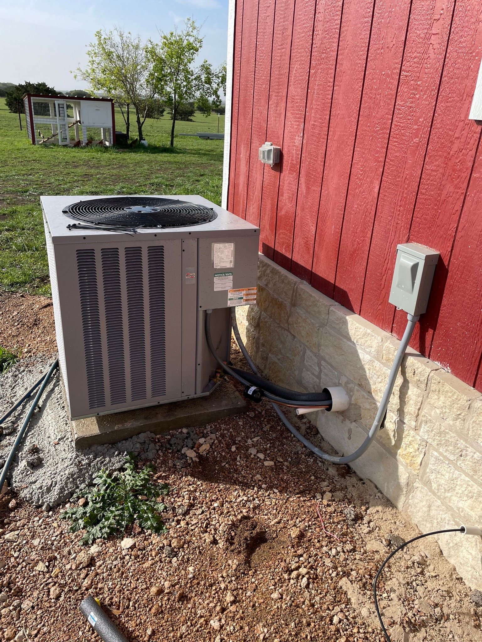 An outdoor air conditioning unit next to a red barn. Gravel ground.