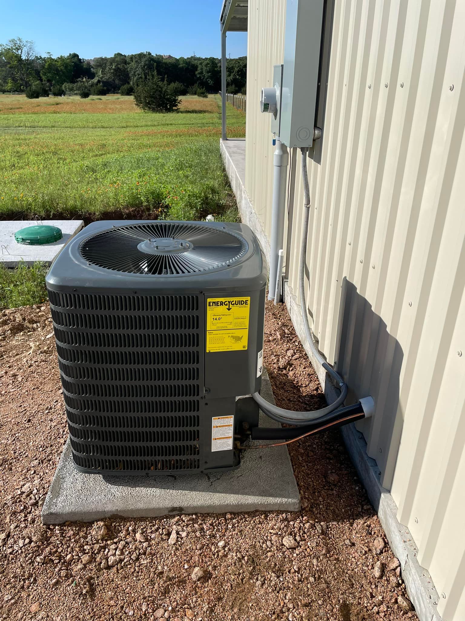 Air conditioner unit outside a building on a concrete pad with surrounding gravel and grass field.