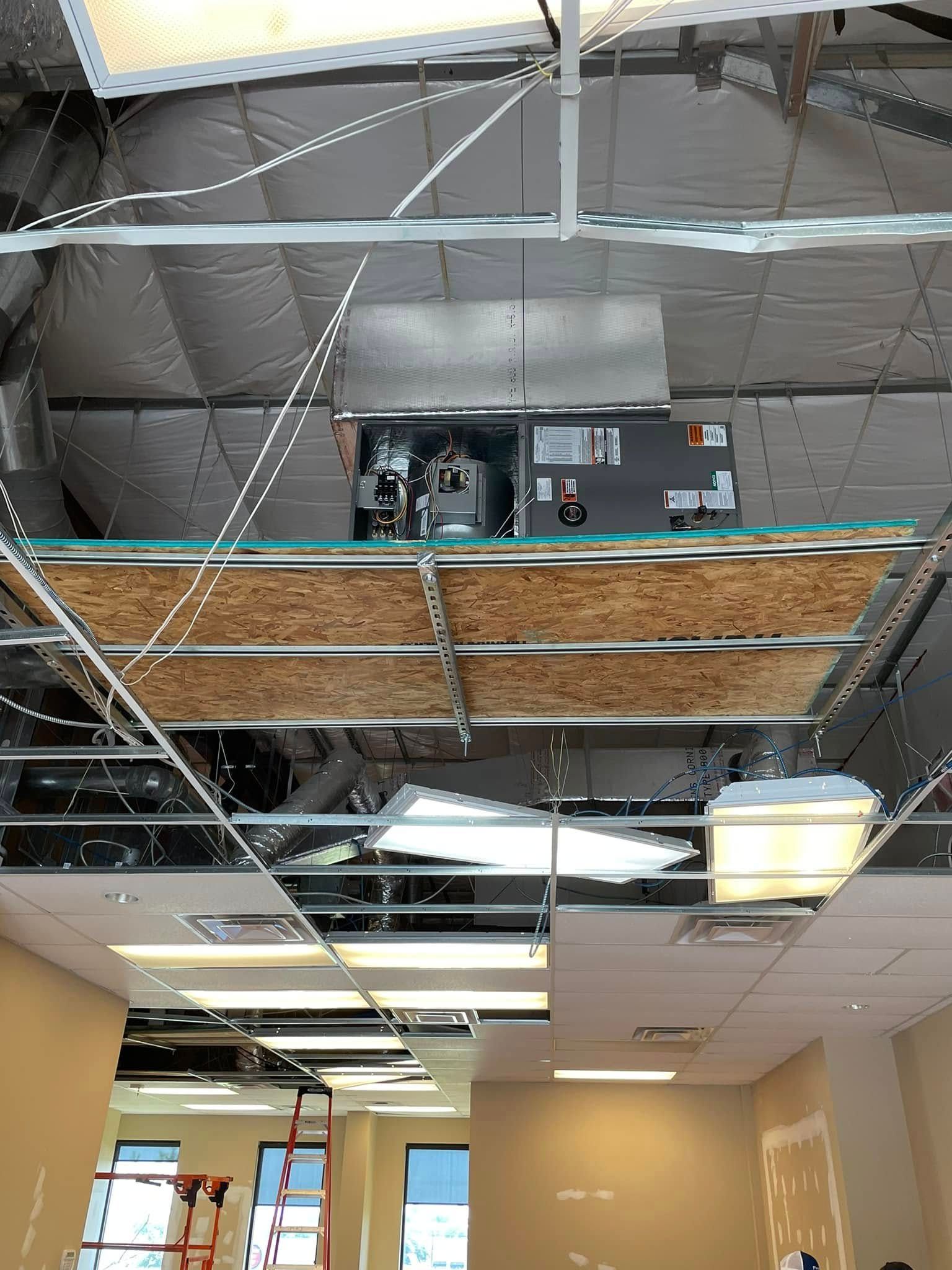 Damaged office ceiling exposing HVAC and insulation. Fluorescent lights and a hallway below.