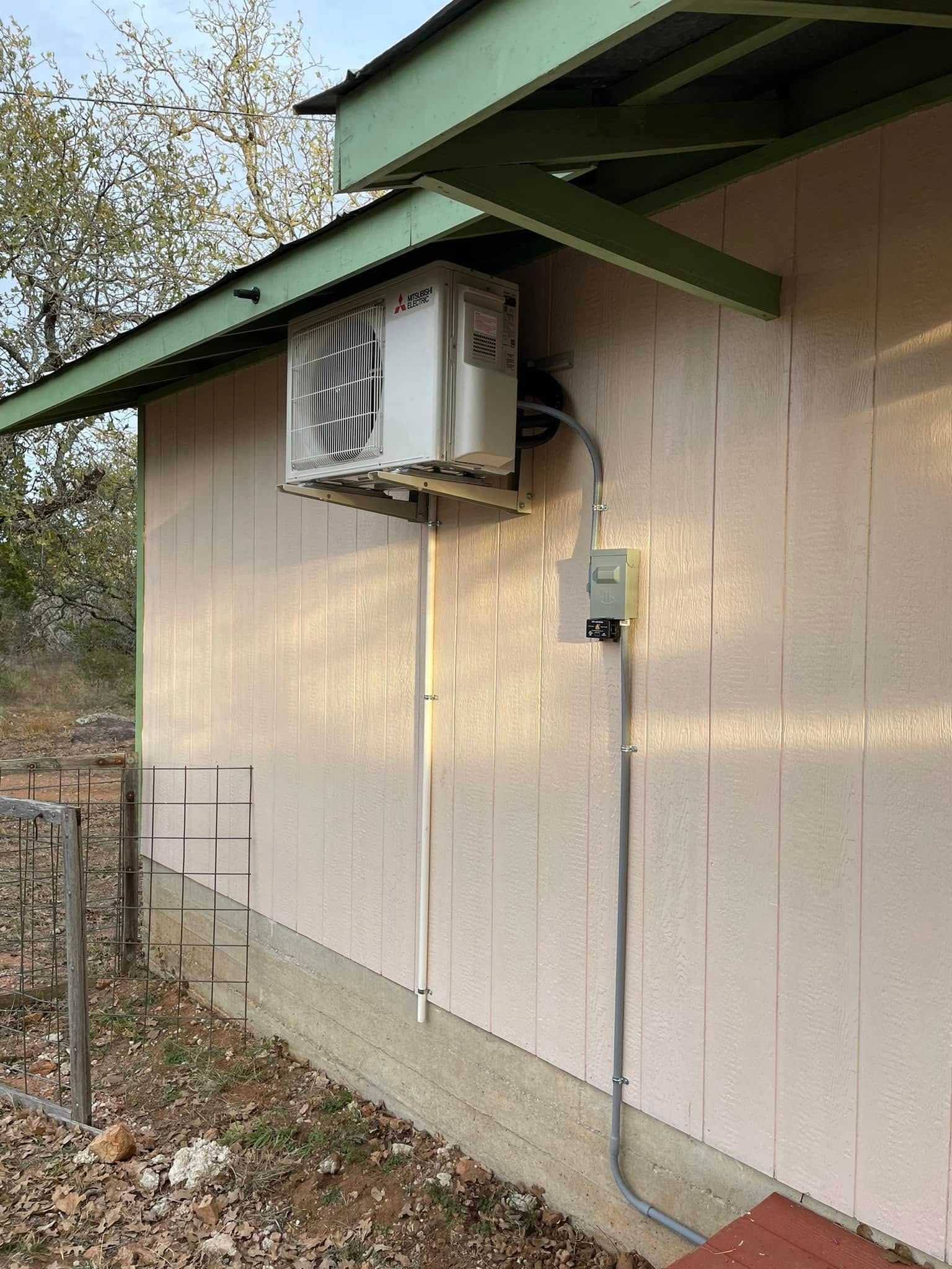 An air conditioner unit mounted on the exterior wall of a pink building with green trim.