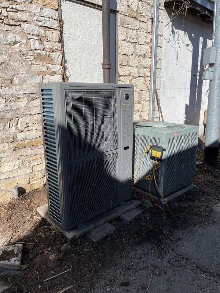 Two air conditioning units outside a stone building. One is gray, the other is green.