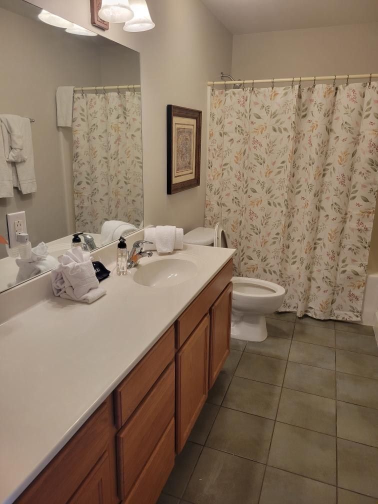 Bathroom with long vanity, mirror, toilet, and floral shower curtain.