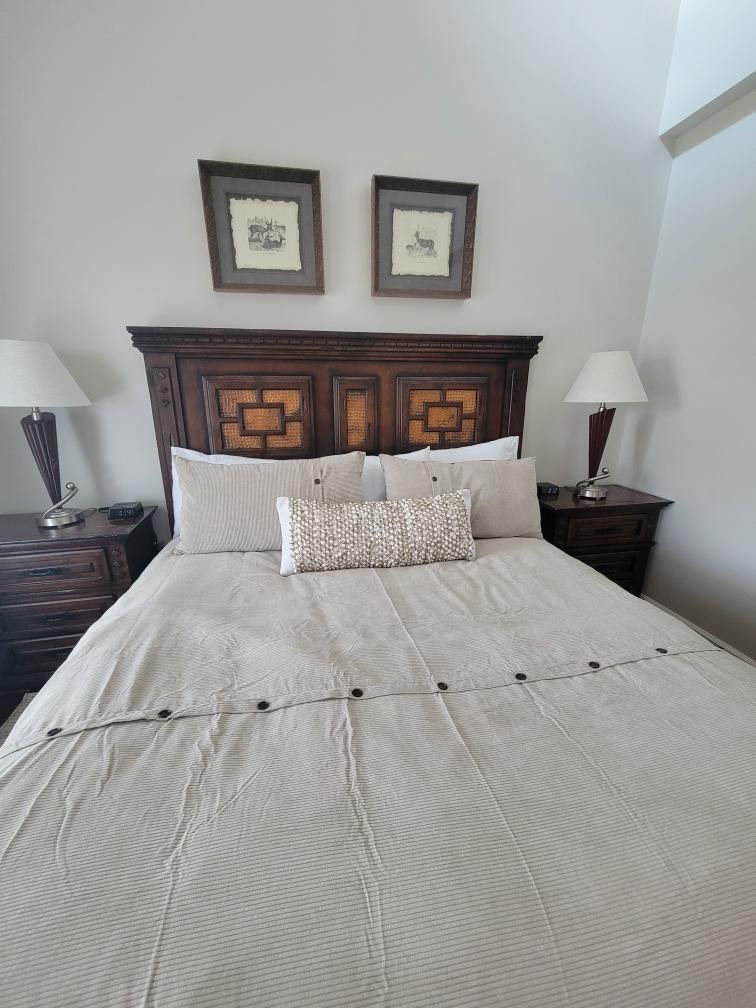 Bedroom with a dark wood headboard, beige bedding, two framed prints, and two bedside lamps.