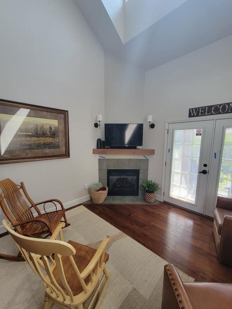 Cozy living room with fireplace, rocking chairs, and a large picture. Natural light streams in.