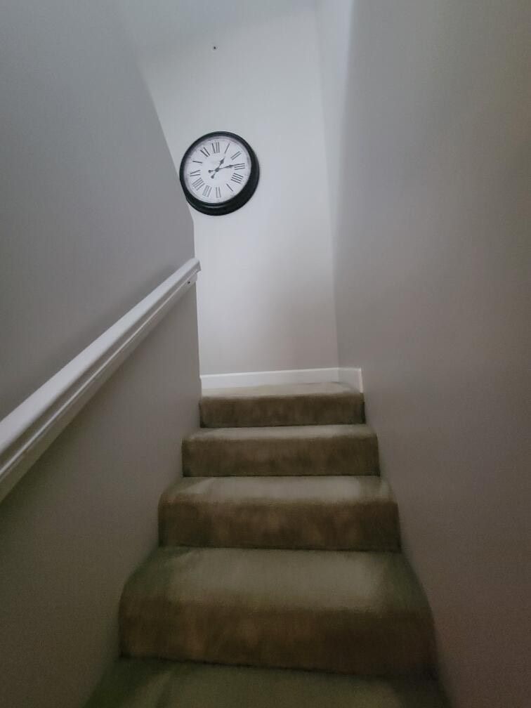 Clock on a wall above carpeted stairs.