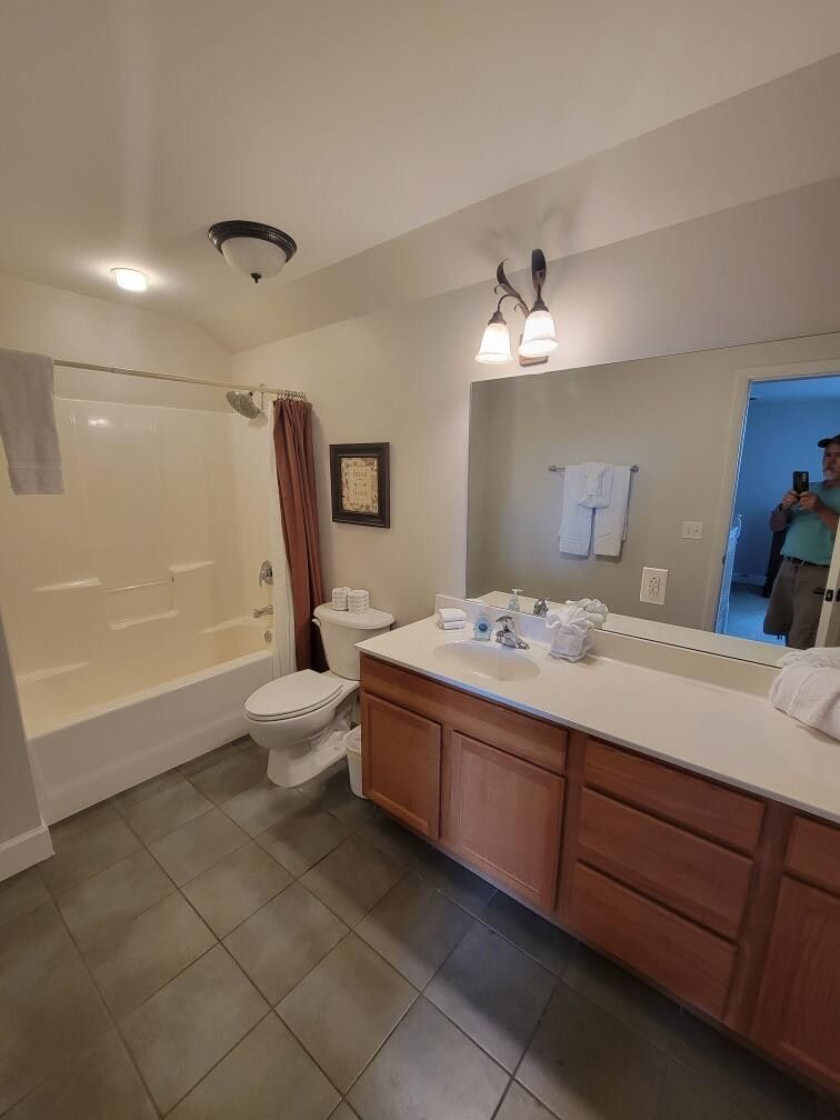 Bathroom with a toilet, vanity, shower/tub, and a person visible in the doorway.