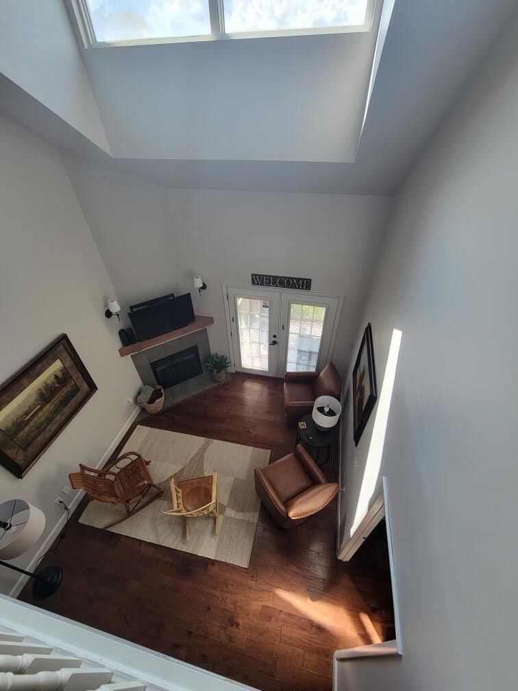 View from above of a living room with a fireplace, chairs, and a rug; natural light through windows.