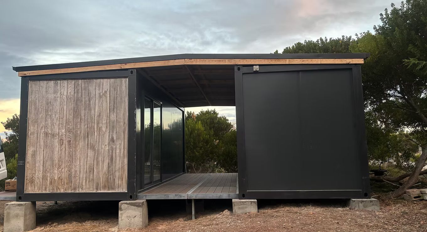 A modern modular structure made from shipping containers with wood cladding, a central deck, and a flat roof outdoors.