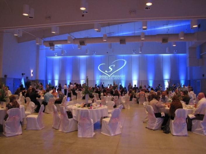 Banquet hall with round tables, seated guests, and a lit stage with blue curtains and a logo backdrop