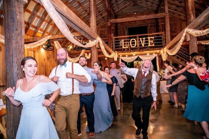Wedding guests dancing in a rustic barn under draped fabric and a glowing “LOVE” sign