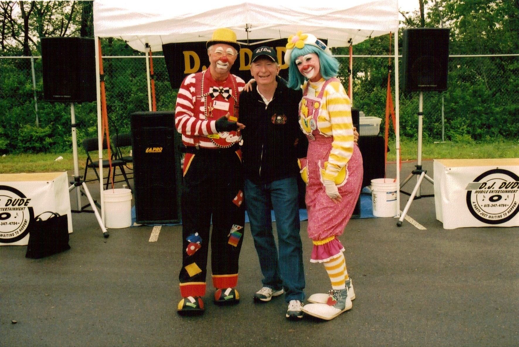 Three people posing under a canopy at an outdoor event, with speakers and banners behind them.