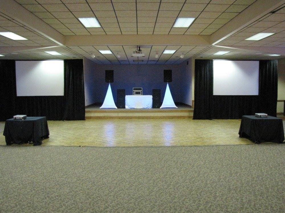 Empty conference stage with two projection screens, tables, and black curtains in a banquet hall