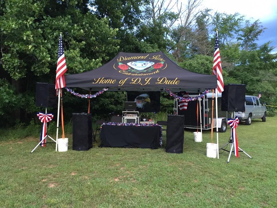 Outdoor memorial setup with black tent, American flags, and tribute banner on a grassy lawn