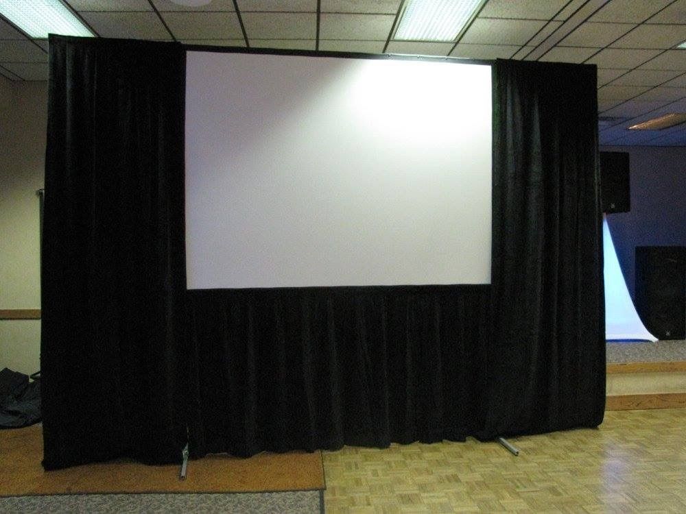 Blank projection screen on a black curtain backdrop in an indoor room
