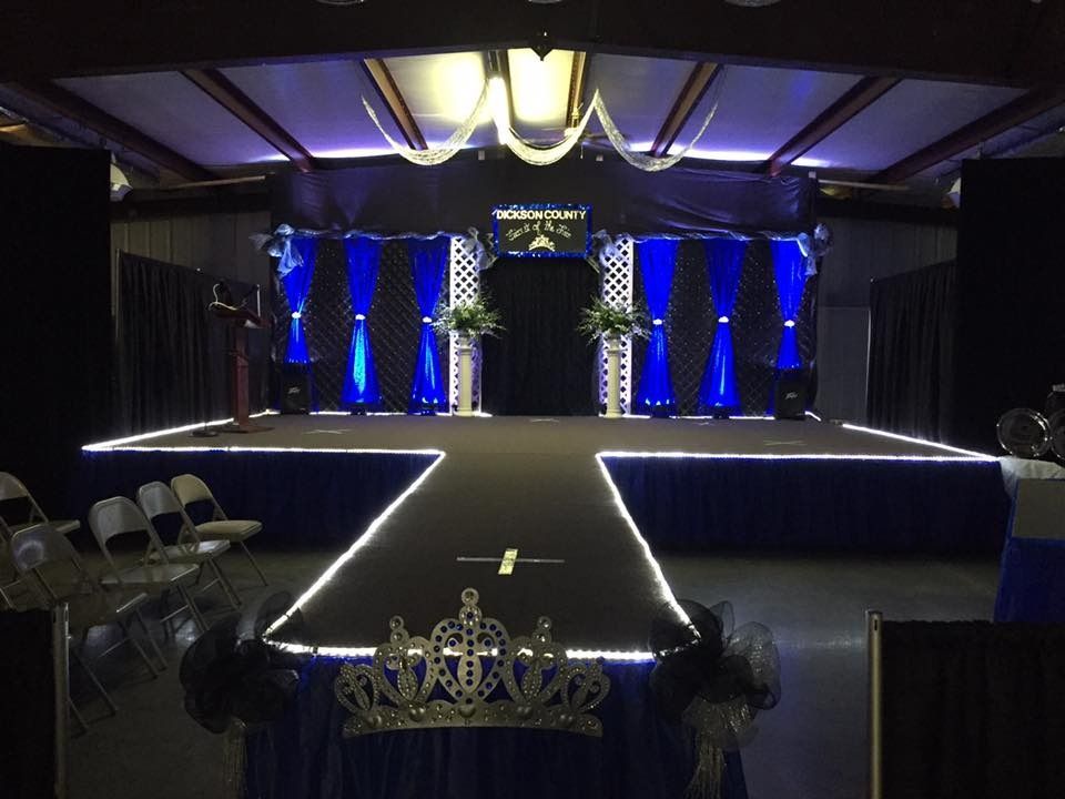 Empty stage with blue-lit columns, black drapes, and a white-edged runway in a banquet hall