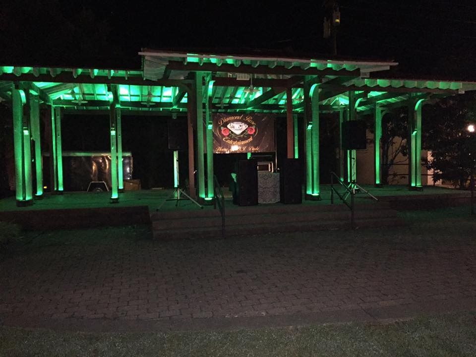 Nighttime view of a pavilion lit with green lights, with a large circular sign at the center.