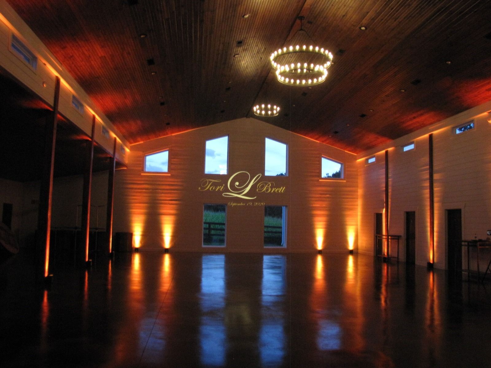 Elegant empty event hall with warm orange uplighting, chandeliers, and a glossy black floor