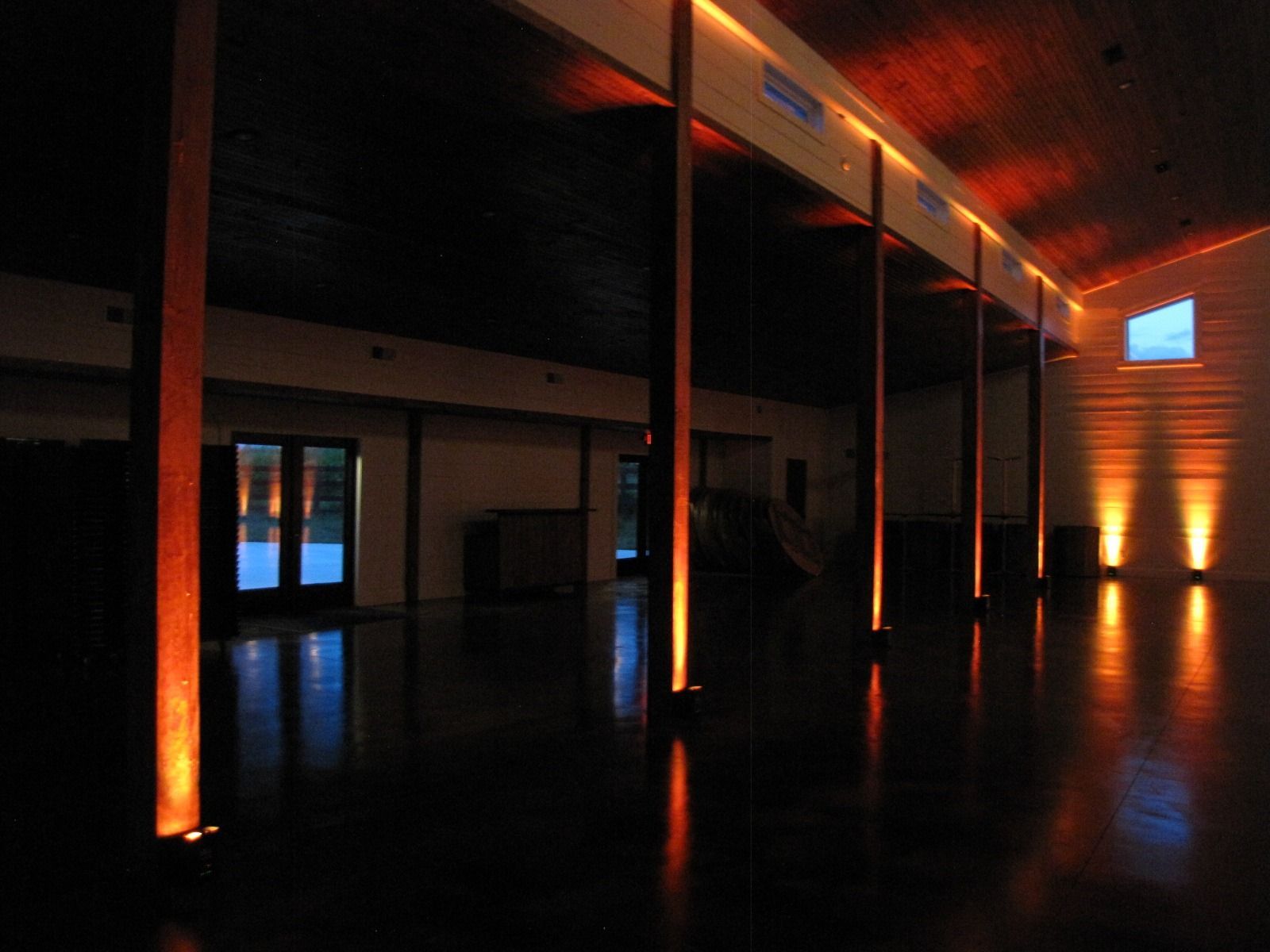 Dimly lit modern hall with orange uplighting, tall columns, and reflective black floor