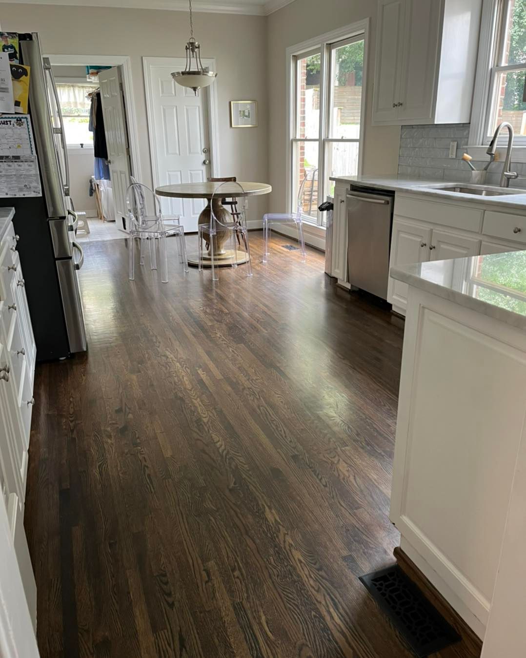A kitchen with hardwood floors , white cabinets , a table and a refrigerator.