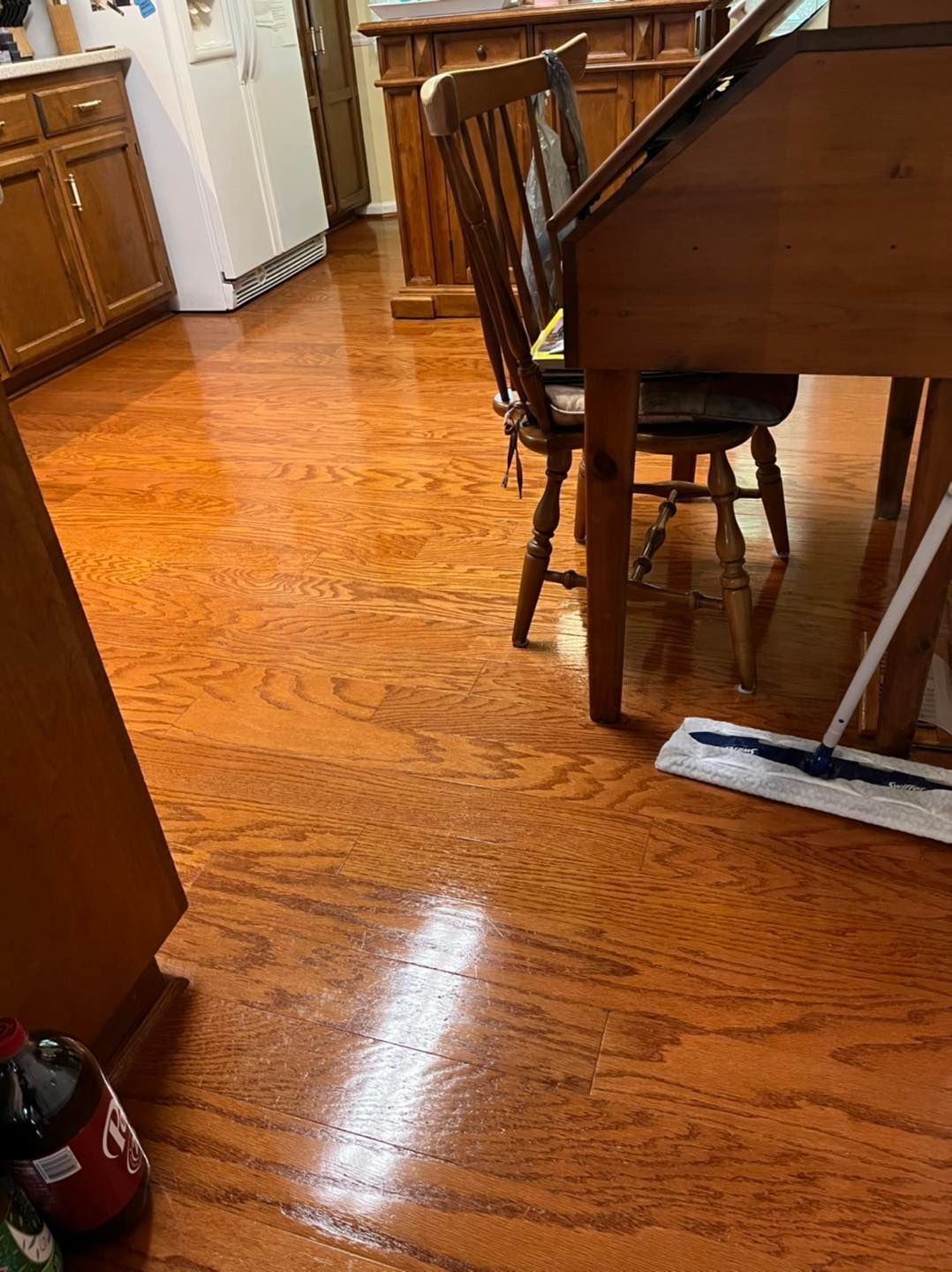 A mop is sitting on a wooden floor in a kitchen next to a table and chairs.