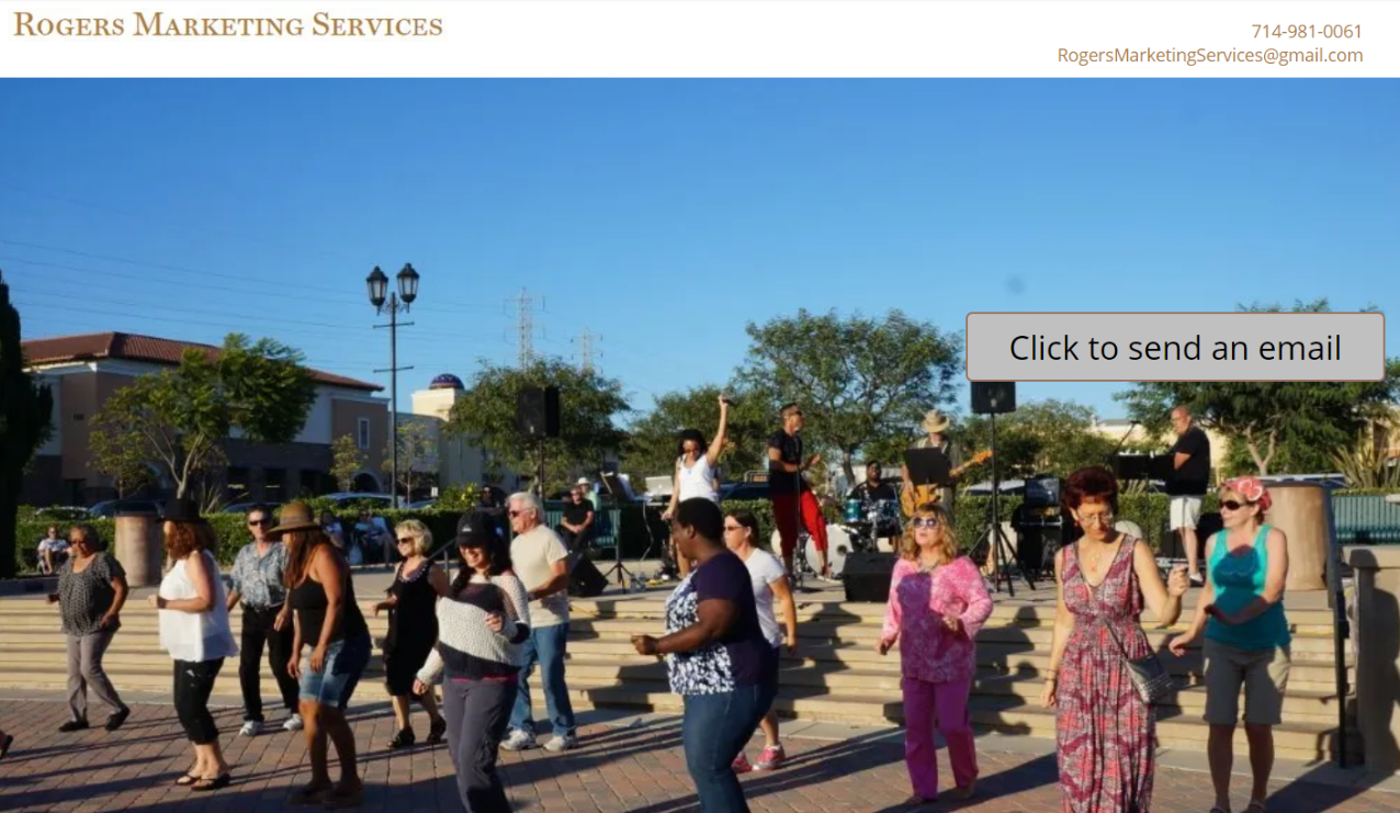 People dancing outdoors in a plaza on a sunny day. Buildings and blue sky in the background.